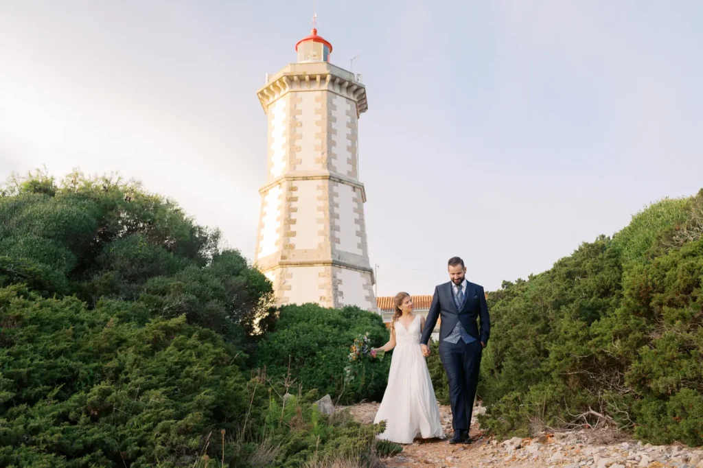 Cascais Guia Lighthouse: A couple walking for the wild cliffs and the Atlantic Ocean having the lighthouse as a background, captured at golden hour light.