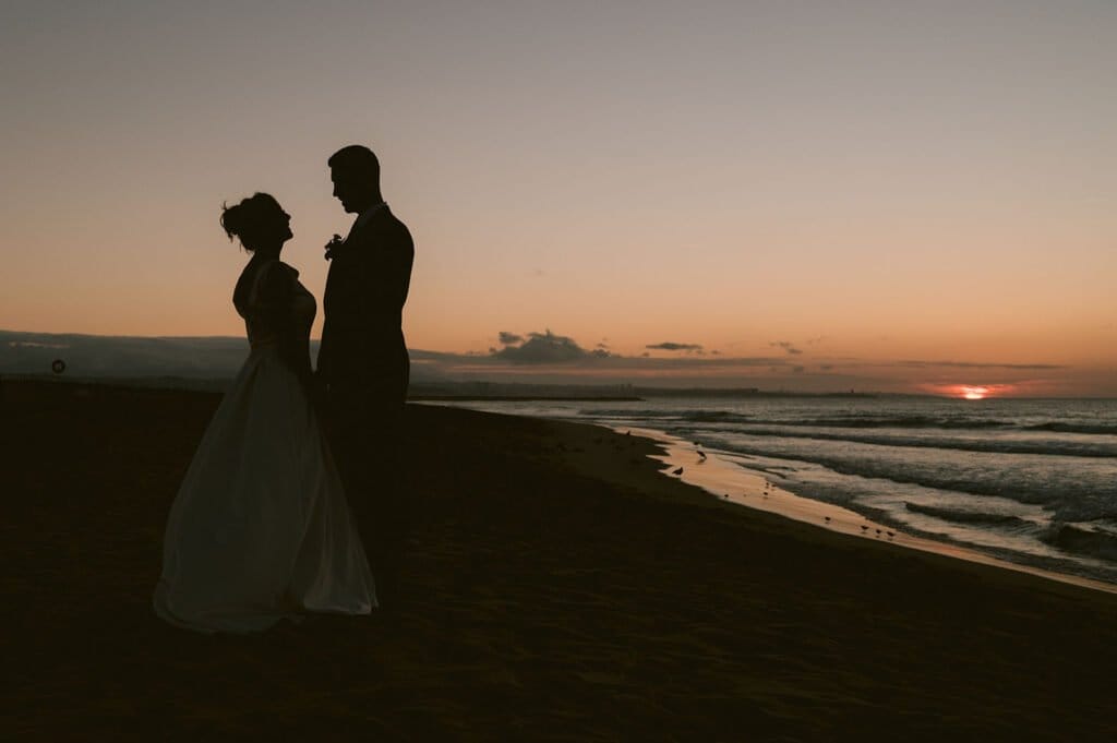 Silhouette of a newlywed couple at the end of the day on Costa da Caparica beach. Barefoot wedding - Beach club.