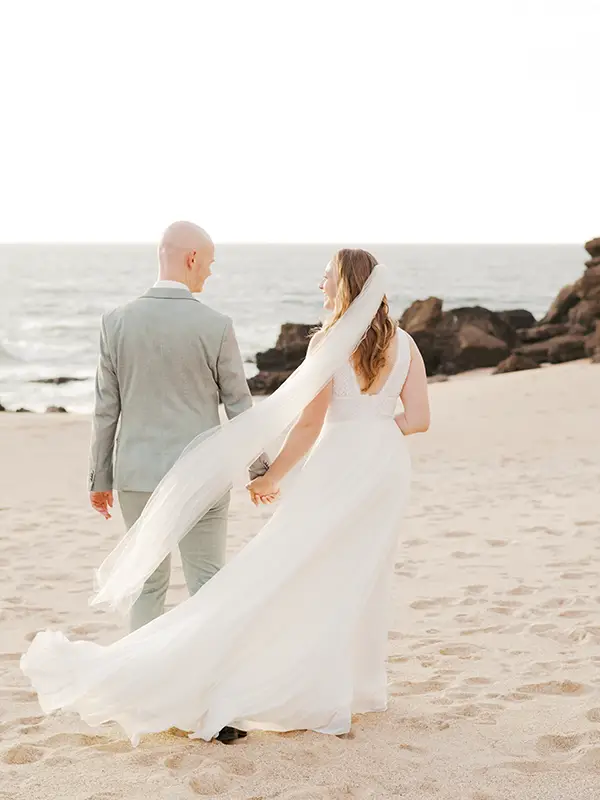 Wedding couple standing hand in hand near the rocks surrounding Forte Guincho Secret Spot in golden sunset light, unposed documentary photography style.