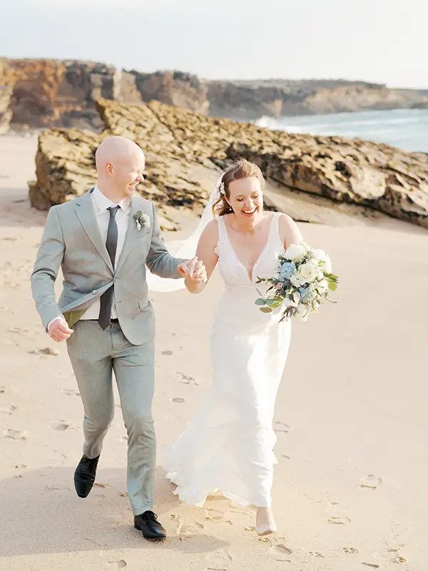 Wedding couple running at the beach close to Forte Guincho Secret Spot in golden sunset light, unposed documentary photography style.