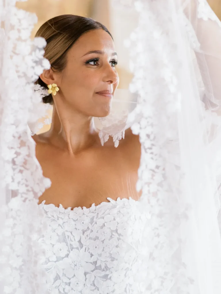 Smiling bride holding a long lace veil in a rustic hall with stone walls, photographed in Portugal by Boris the Cat