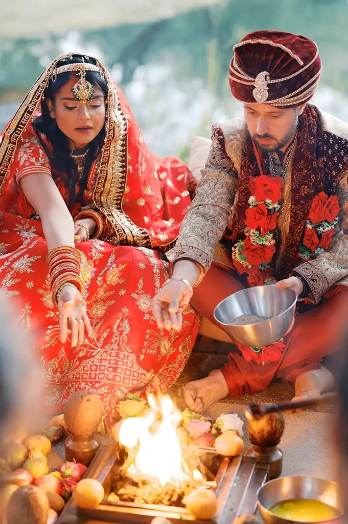 Happy and smiling couple during the sacred rituals of the Hindu wedding ceremony under a lush floral Mandap at a palace in Sintra.