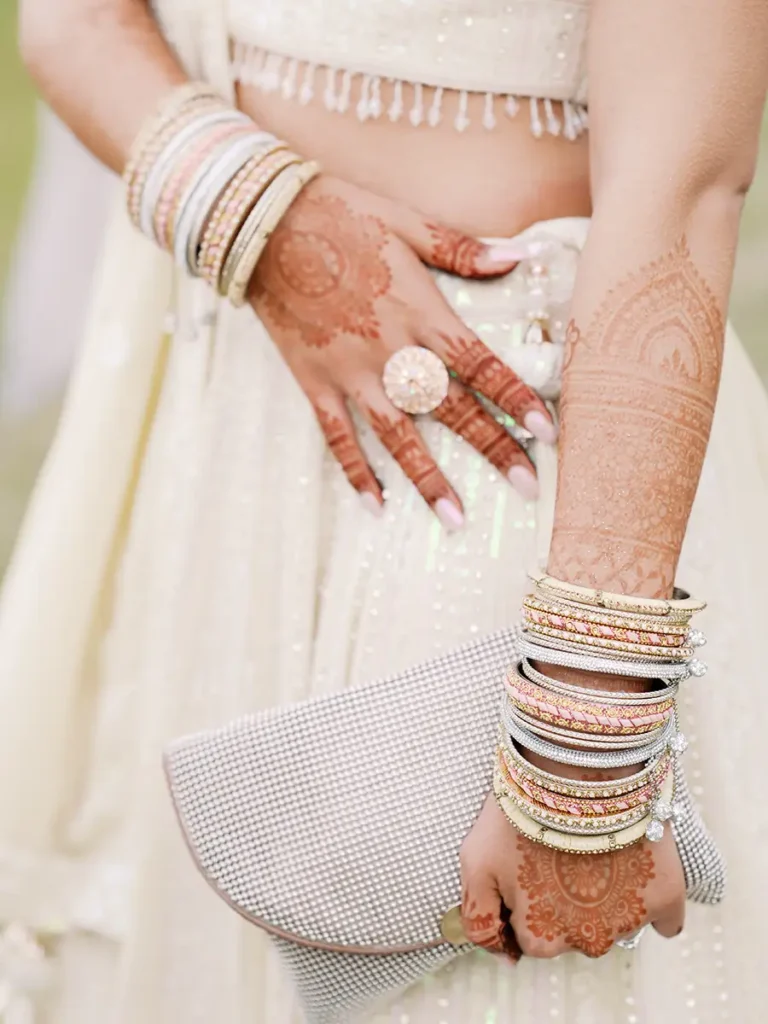 Fine Art detail photography of a Hindu bride's hands with deep Mehndi designs, holding an elegant purse surrounded by traditional jewelry.