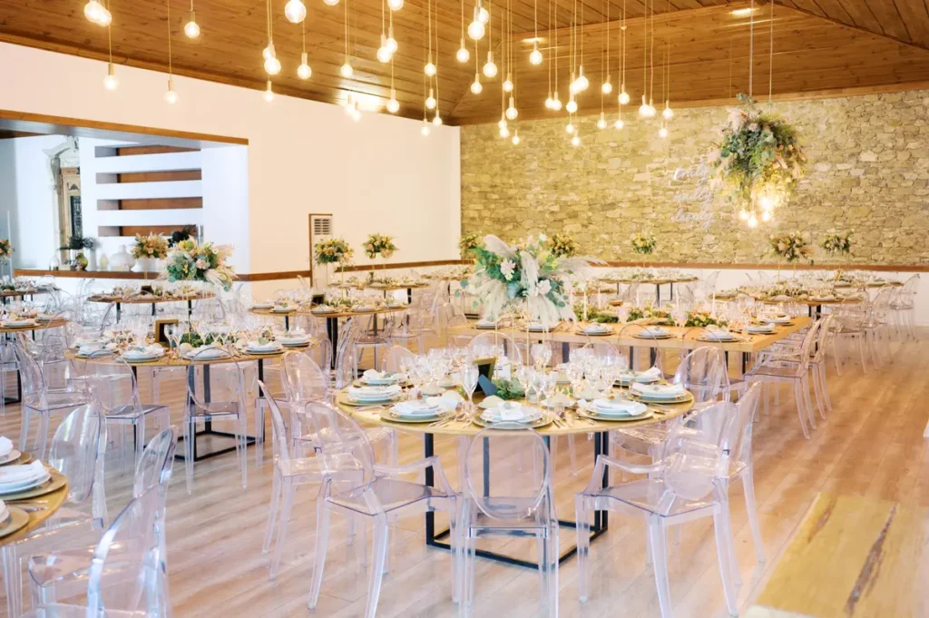 Vista interior do salão de banquetes na Quinta da Bichinha, com teto de madeira, iluminação suspensa moderna e mesas redondas decoradas em tons rústico-chiques.