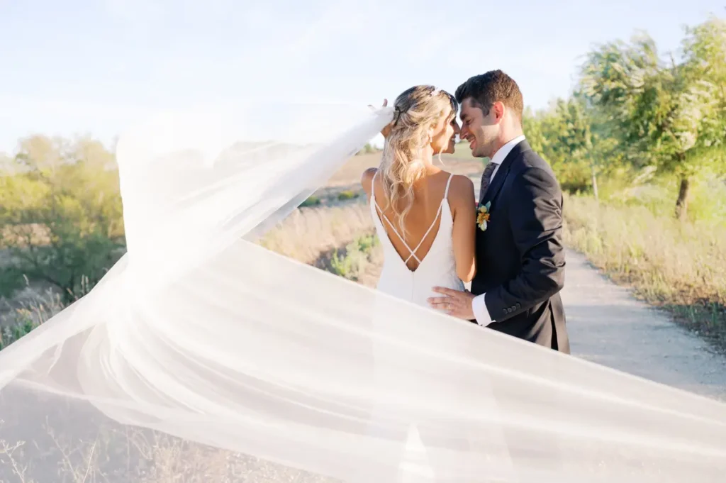 Romantic portrait of the bride and groom at Quinta da Bichinha with the veil blowing in the wind, taking advantage of the natural light and the vineyard and garden landscapes in Alenquer.