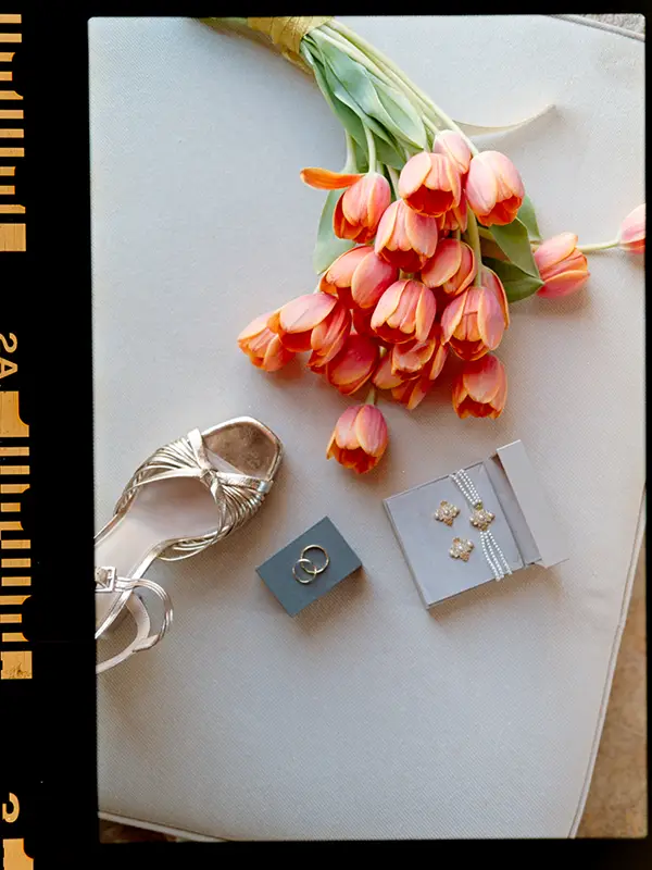 Flat lay of bridal details with a tulip bouquet, golden sandal, wedding rings, and jewelry, shot on 35mm analogue film by Boris the Cat.