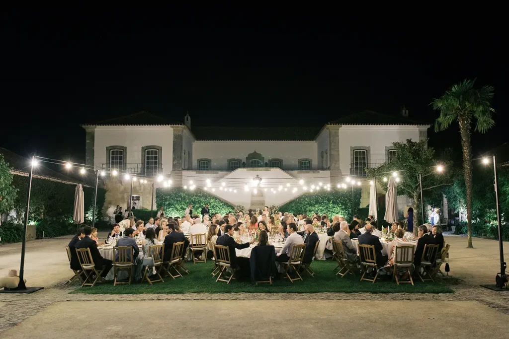Elegant outdoor wedding dinner setup with festoon lights glowing at dusk in the Portuguese countryside.